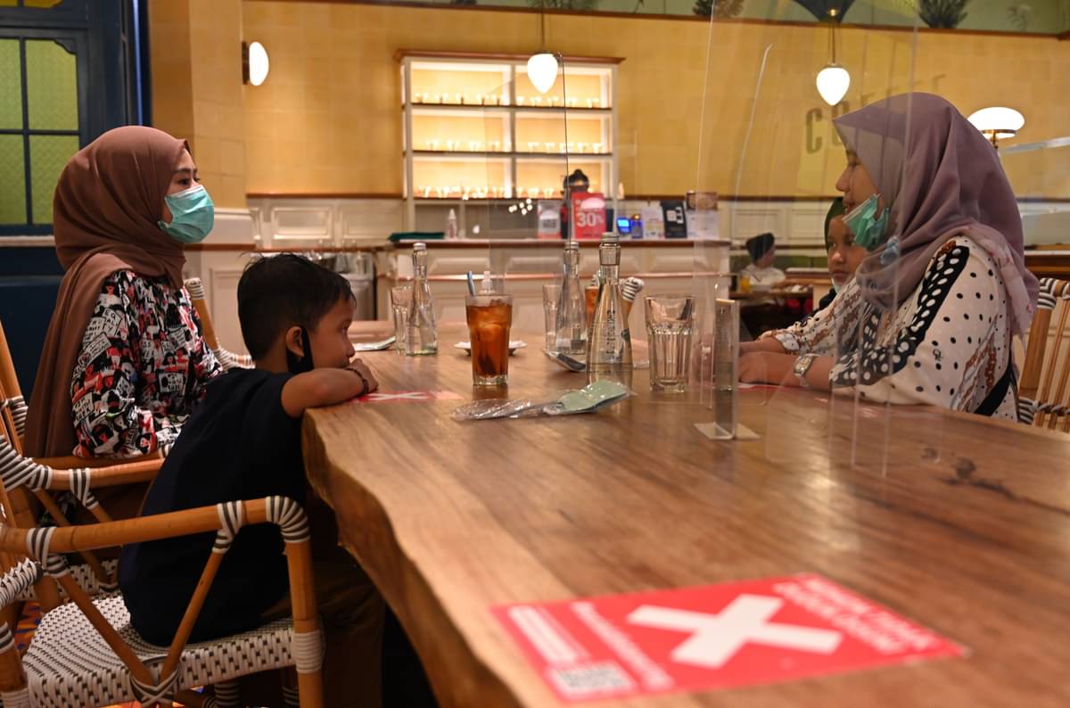 Warga mengenakan masker duduk di meja sebuah restoran yang dipisahkan partisi plastik.