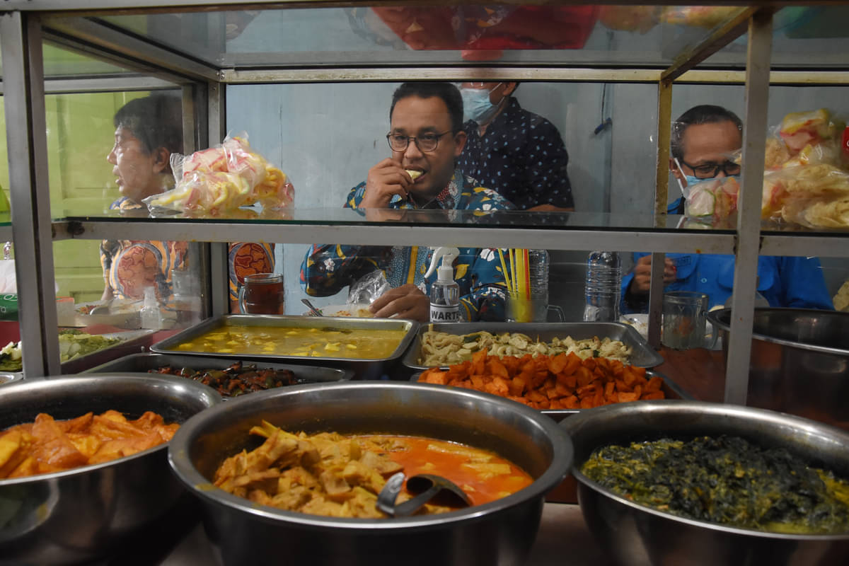 Gubernur DKI Jakarta Anies Baswedan (tengah) menikmati makan siang di salah satu warteg.