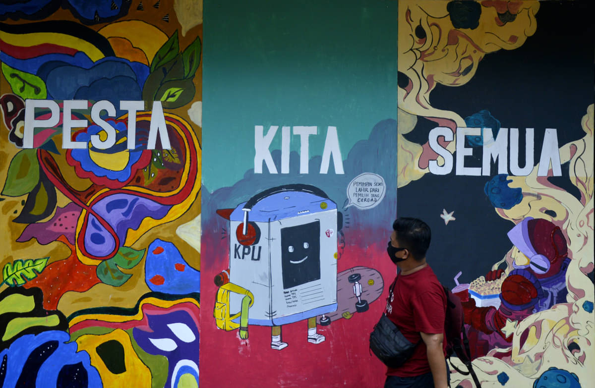 Warga melintasi mural terkait pemilu di wilayah Makassar.