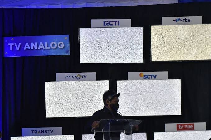 Seorang panitia melintas di dekat layar siaran televisi analog yang telah dihentikan