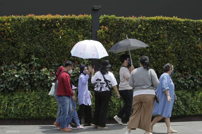 Pejalan kaki berlindung dari sengatan matahari saat melintasi pedestrian di kawasan Thamrin, Jakarta.