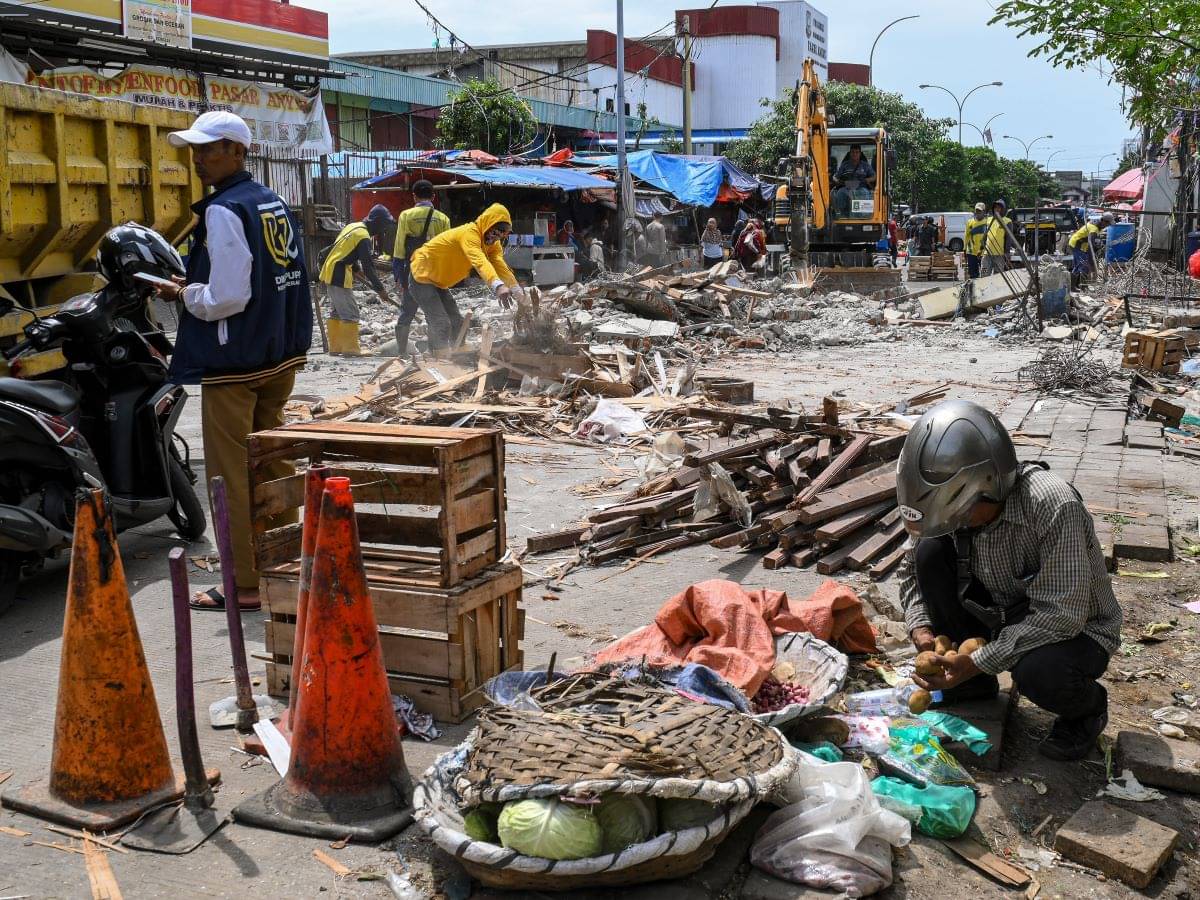 Pedagang memindahkan barang dagangan dengan latar belakang petugas menggunakan alat berat membongkar gapura Pasar Anyar di Tangerang.