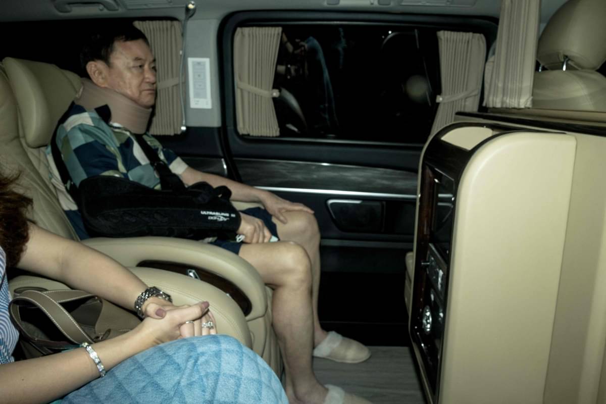 Thaksin Shinawatra mengenakan penyangga leher dan duduk di samping putrinya, terlihat melalui jendela mobil meninggalkan rumah sakit polisi.
