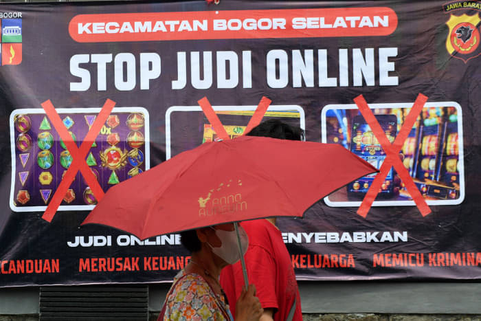 Warga berjalan di depan spanduk sosialisasi larangan judi online.