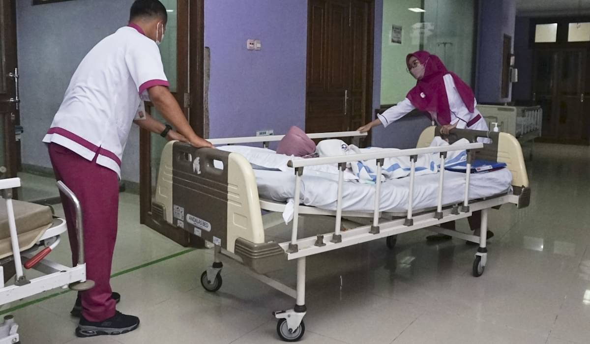 Petugas kesehatan mendorong tempat tidur pasien di rumah sakit 