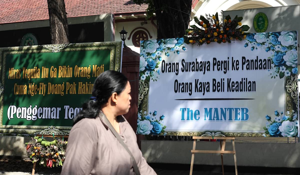 Warga berjalan di dekat karangan bunga yang terpajang di depan Gedung Pengadilan Negeri Surabaya 