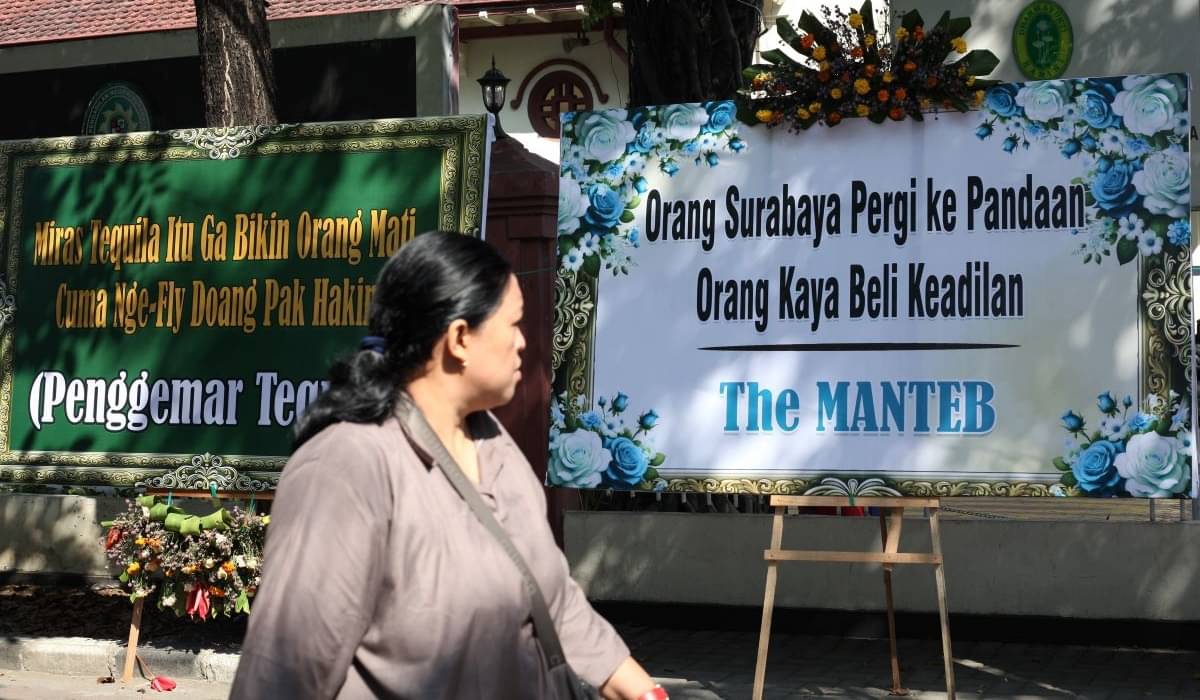 Warga berjalan di dekat karangan bunga yang terpajang di depan Gedung PN Surabaya, Jalan Arjuno, Surabaya, Jawa Timur, Senin (29/7).